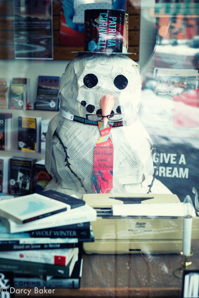 window of a book store with a snowman made of newspaper sitting at an old typwriter